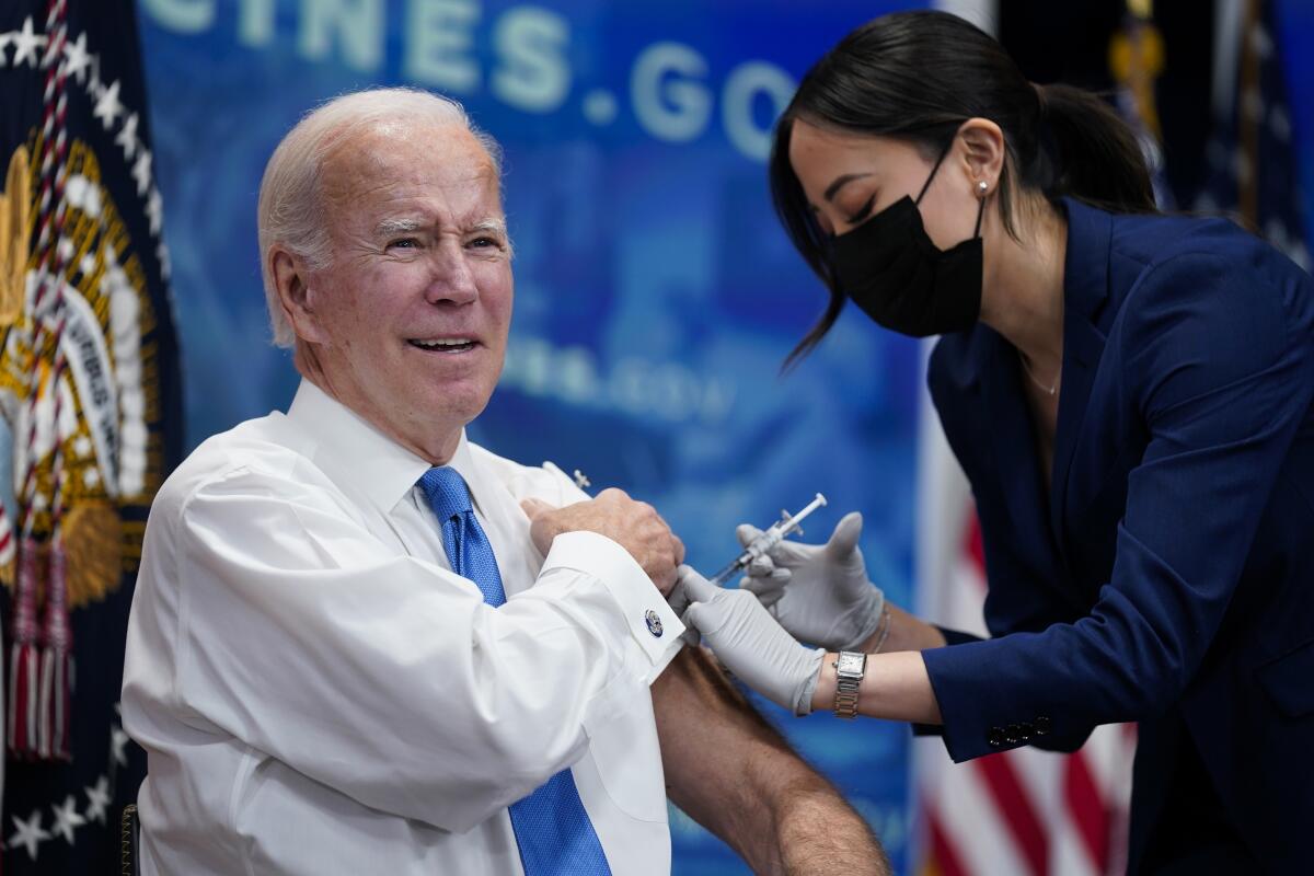A healthcare worker gives a vaccine to a smiling President Biden.