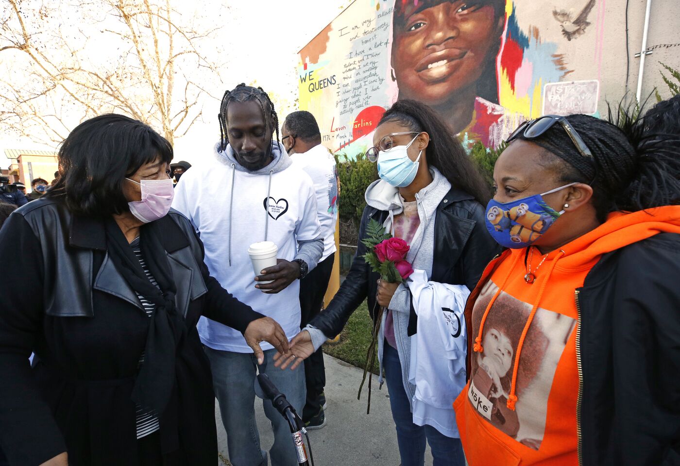 People stand around in front of a mural of a girl.