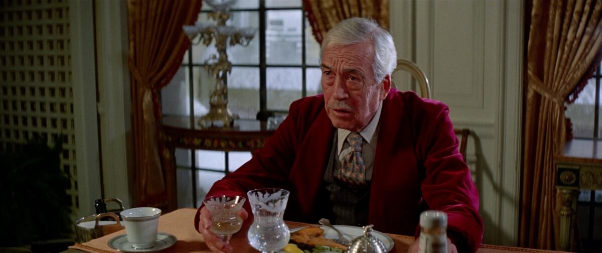 A man in a red jacket sits at a dining-room table.
