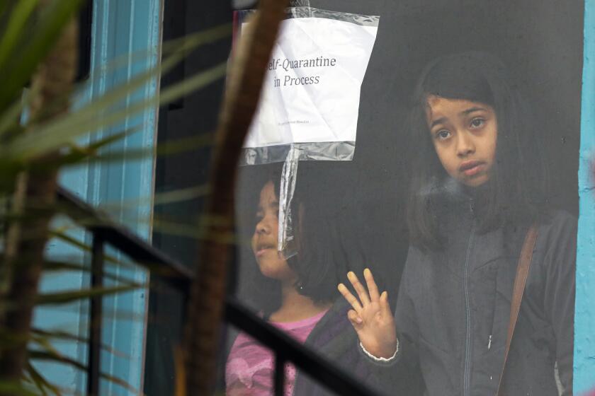 LOS ANGELES, CA - MARCH 14, 2020 - Two sisters Meztli Escudero, 8, left, and Victoria Escudero, 10, stand in the window of a vacant house, they and their have occupied on Saturday morning. Impacted by the housing crisis, and feeling even more urgency in the wake of the Coronavirus pandemic, a group of families who need safe and healthy housing went to "reclaimed" 6 vacant houses owned by the state in the El Sereno neighborhood of Los Angeles. The vacant properties are currently owned by Caltrans, purchased decades ago as part of the now aborted 710 freeway expansion. Over 200 now sit vacant while thousands live on the streets of Los Angeles County. (Irfan Khan / Los Angeles Times)