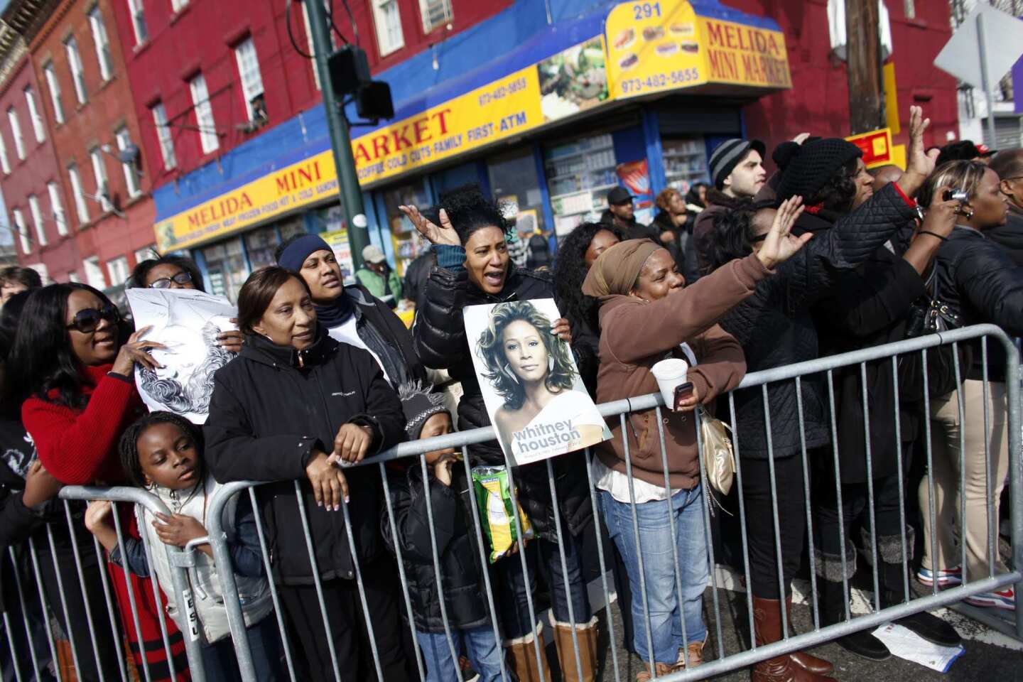 Whitney Houston fans wave to a passing car as they gather a few blocks from the New Hope Baptist Church in Newark, N.J.