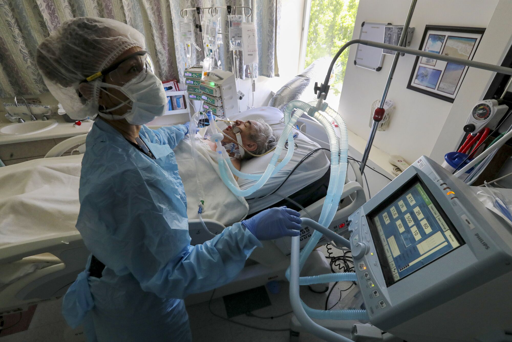 A nurse checks a monitor next to a patient who has an oxygen tube.