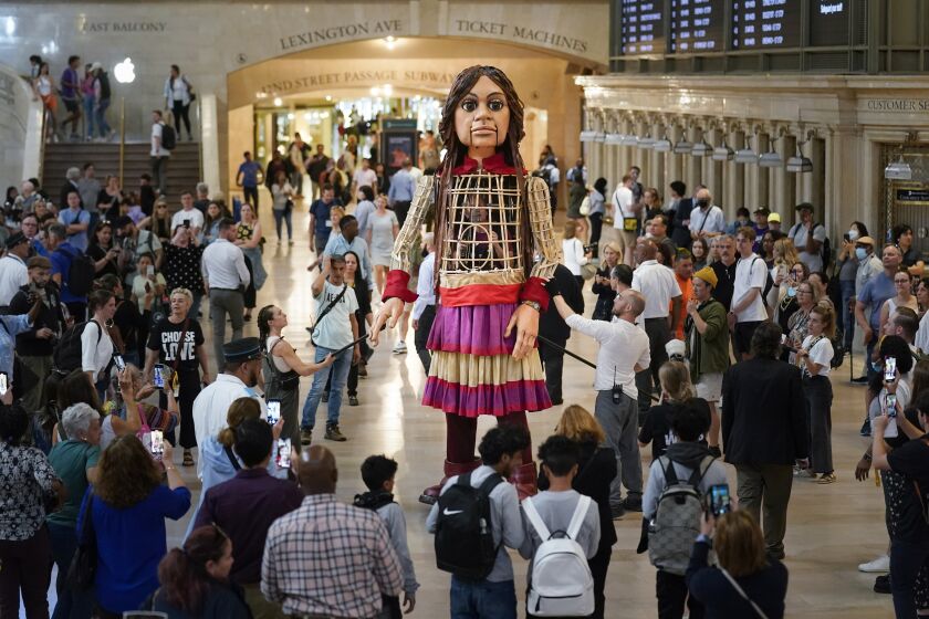 Commuters and tourists gather around a large puppet named Little Amal as she walks around Grand Central Station in New York, Thursday, Sept. 15, 2022. New York City's latest celebrity visitor is stopping traffic even in this jaded, larger-than-life town. Little Amal, a 12-foot puppet of a 10-year-old Syrian refugee, is on a 17-day blitz through every corner of the Big Apple as part of a theater project hoping to raise awareness about immigration. (AP Photo/Seth Wenig)
