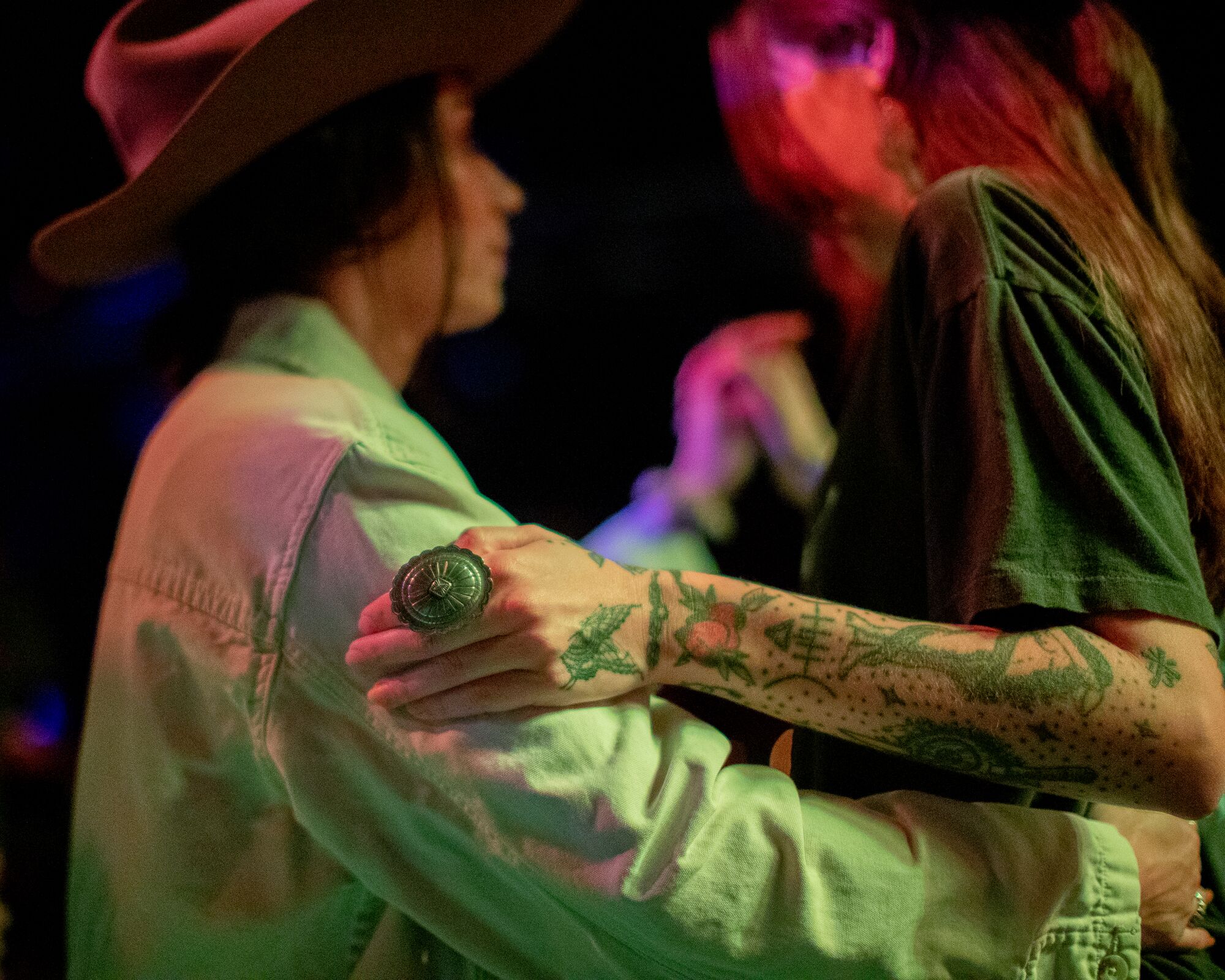 A detail of two people dancing, showing a person's hand adorned with tattoos and a large oval ring.