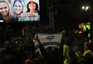 A person holding an Israeli flag in front of a screen with three women.