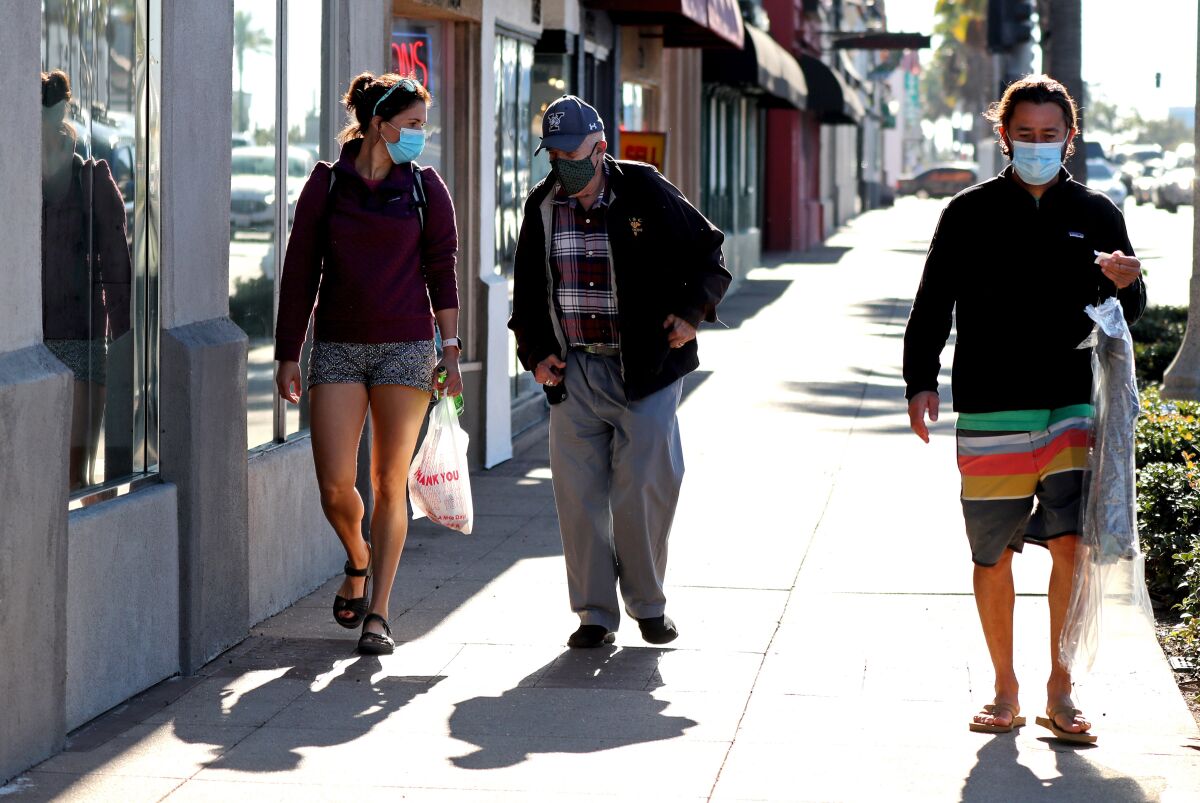 People walk outside wearing masks along Newport Boulevard.