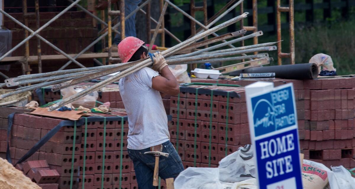 A worker carries scaffolding poles on a home site in Virginia.