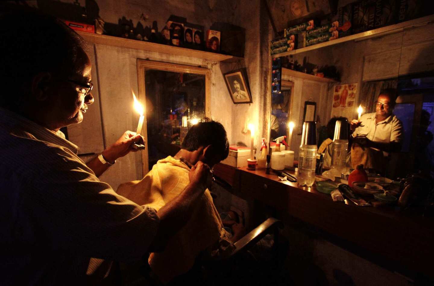 A barber gives a haircut by candlelight at his shop in Kolkata. India's energy crisis cascaded over half the country Tuesday when three of its regional grids collapsed, leaving 620 million people without electricity.