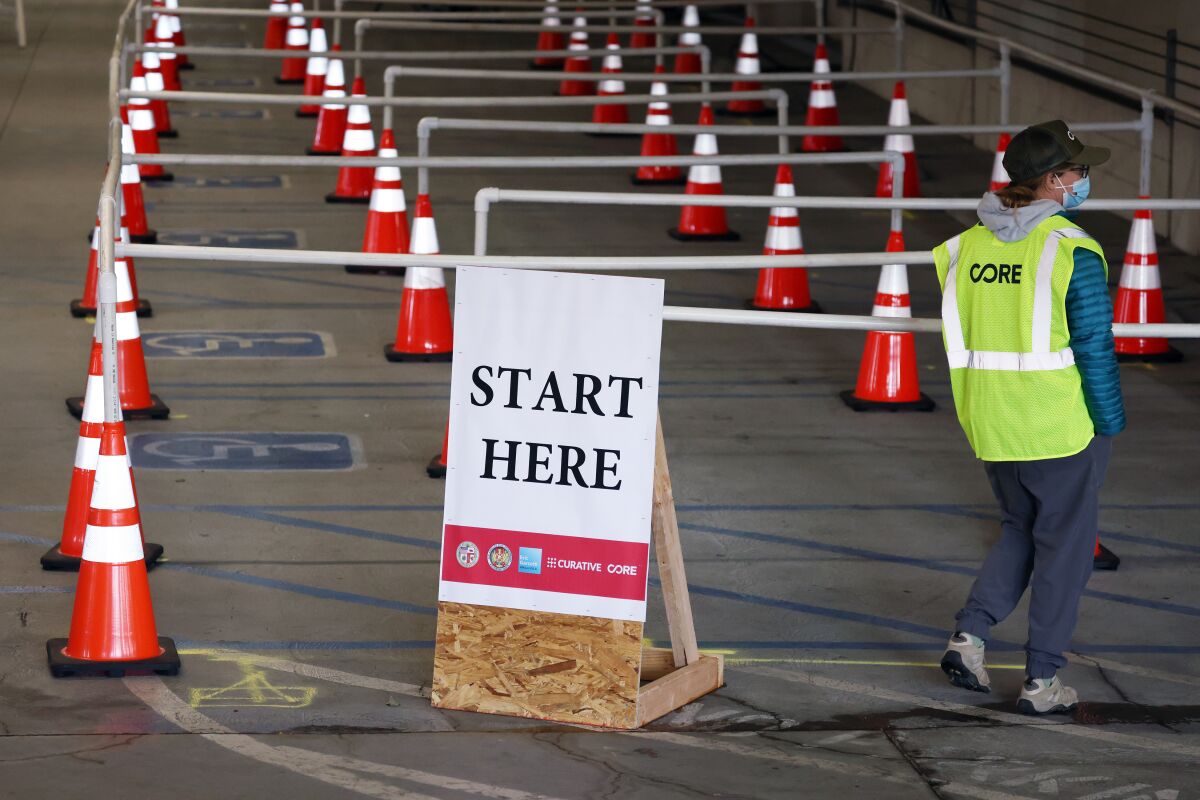 Cones mark the lines at a COVID-19 vaccination site. A sign reads "Start here."