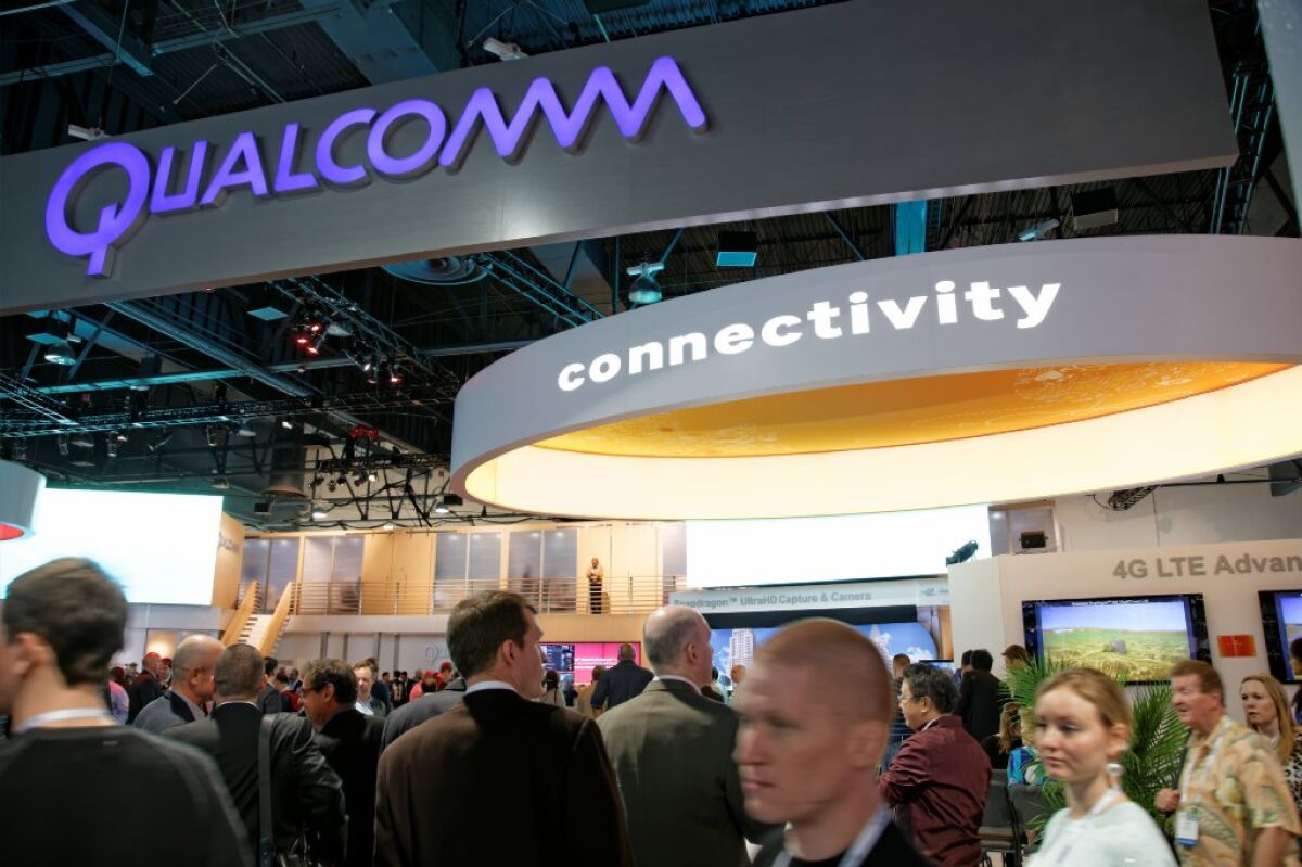 People at a trade show pass beneath signs reading "Qualcomm" and "connectivity."