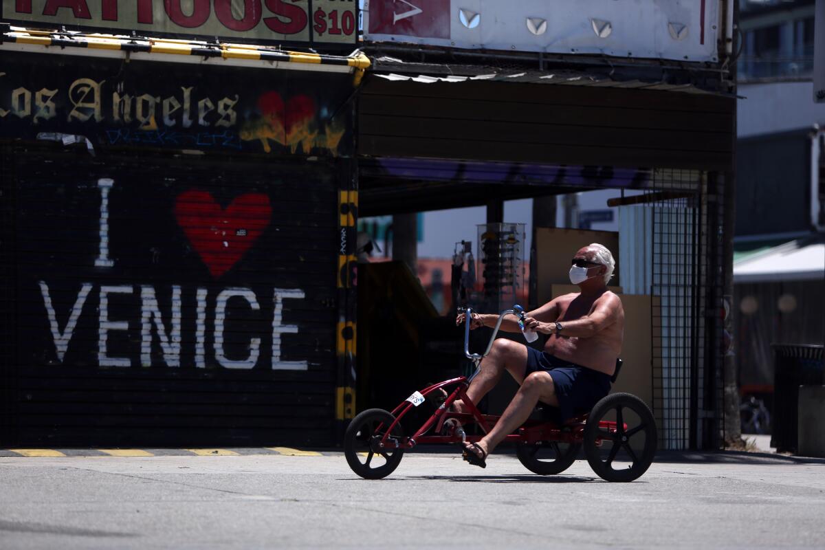 A man wears a mask while riding a tricycle along the boardwalk in Venice.