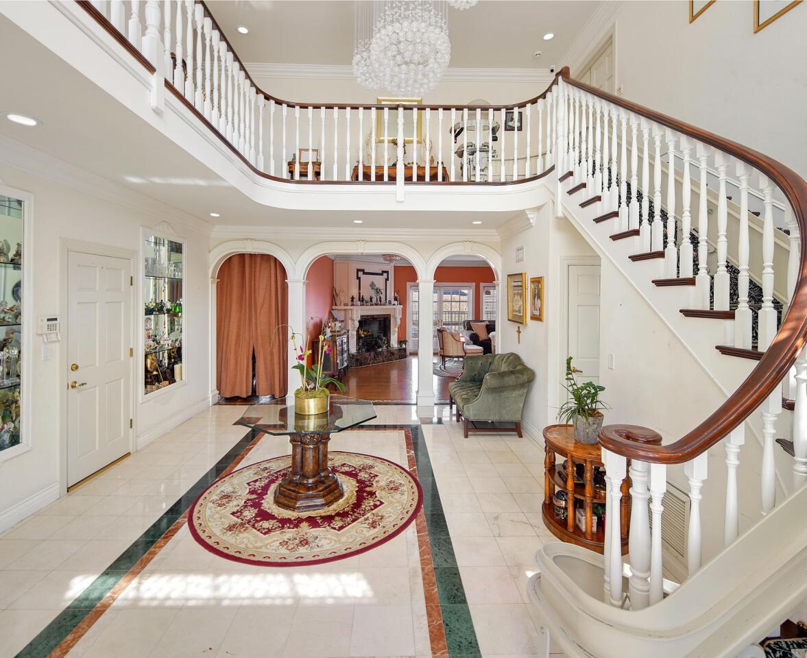 The foyer is white with a staircase, railing and furnishings.