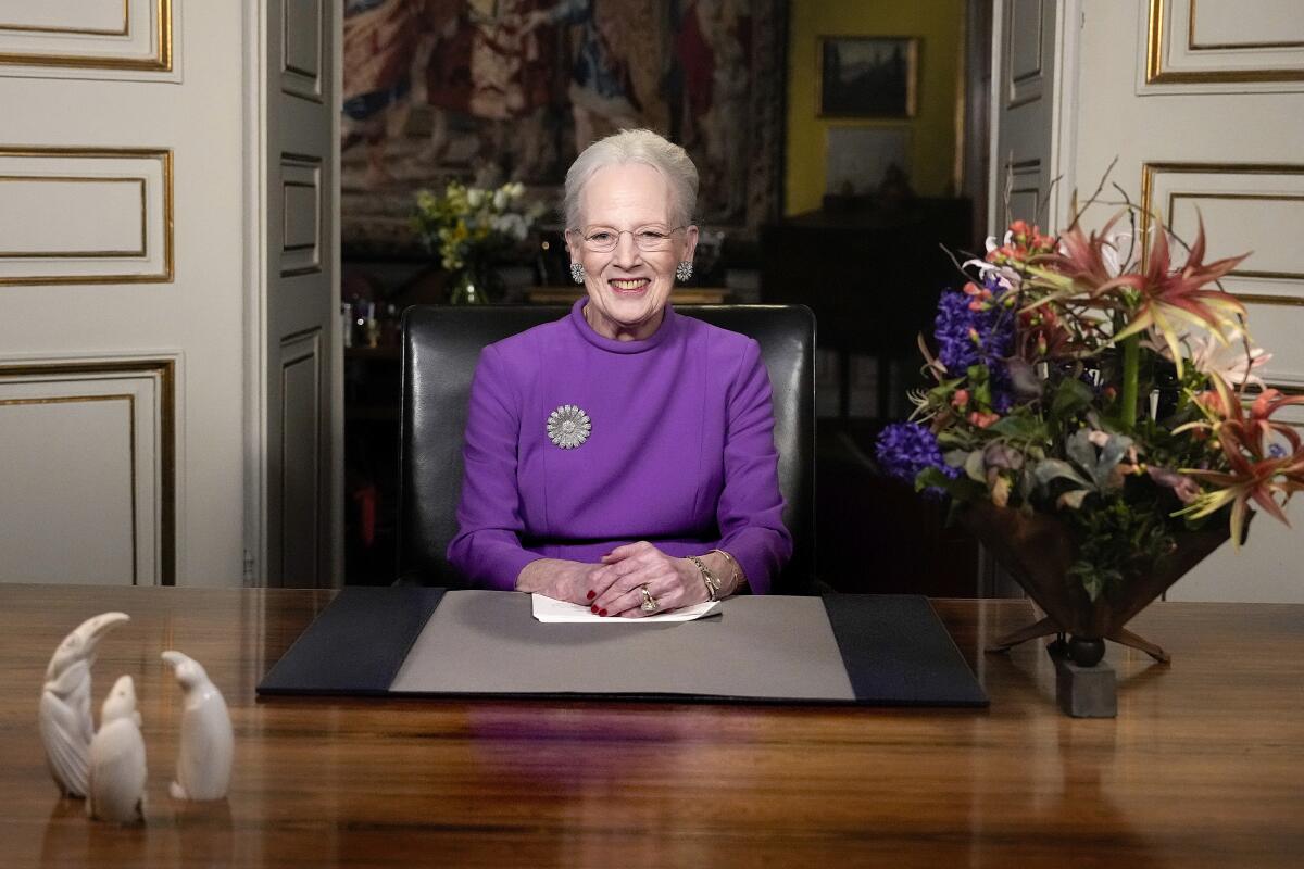 Queen Margrethe II sits at a desk with a vase of flowers next to her.