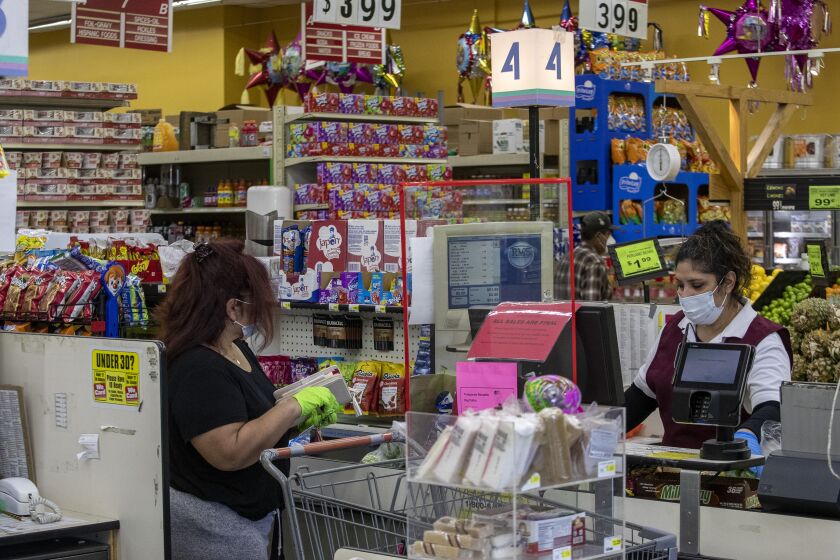 WEST ADAMS, CA - APRIL 04: A supermarket cashier wears a mask to guard against the coronavirus as she scans grocery items at the Advance Food Market on Saturday, April 4, 2020 in West Adams, CA. (Brian van der Brug / Los Angeles Times)