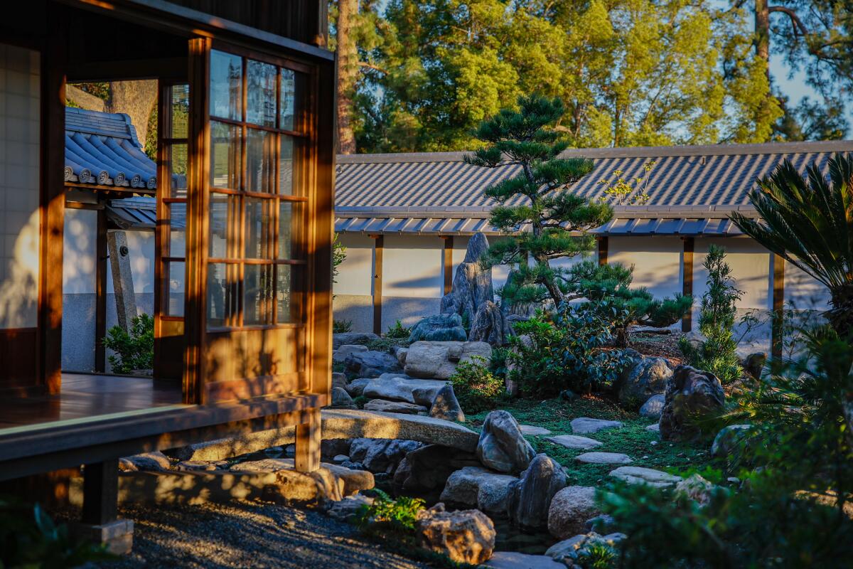 A traditional Japanese-style garden and buildings in dappled sunlight