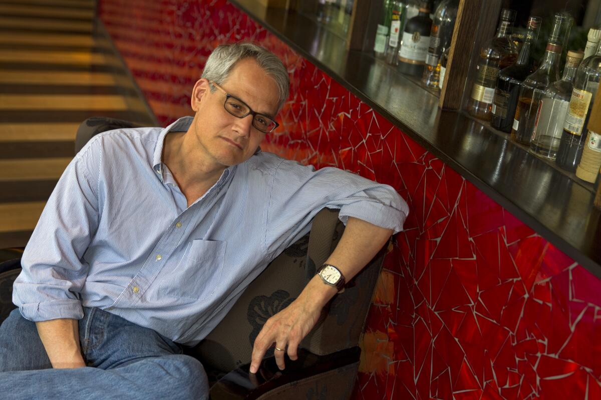 A portrait of Blake Bailey, seated and wearing a button-down shirt with rolled-up sleeves.