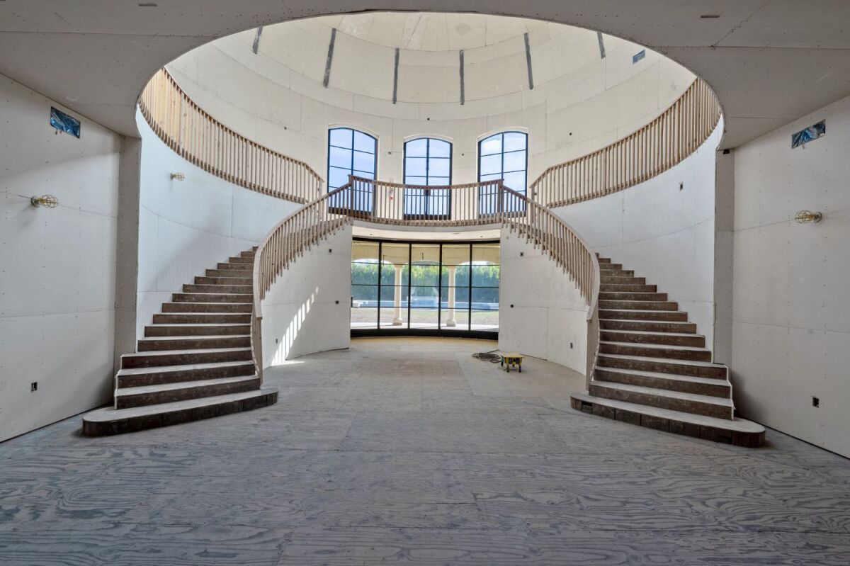 An unfinished foyer inside a mansion with staircases on either side and large windows