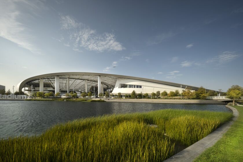The curling roofline of Sofi Stadium can be seen behind a lake with wetland areas.