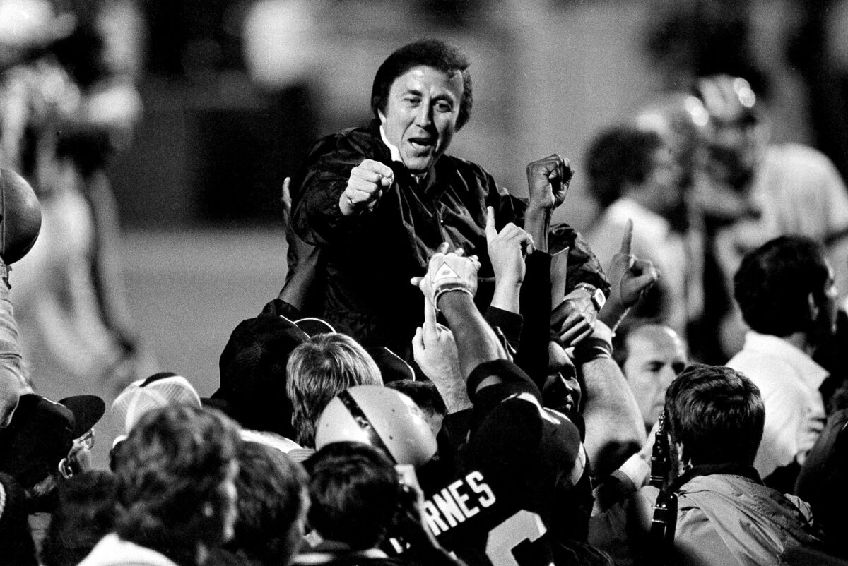 Coach Tom Flores holds out a fist as Raiders football players lift him up