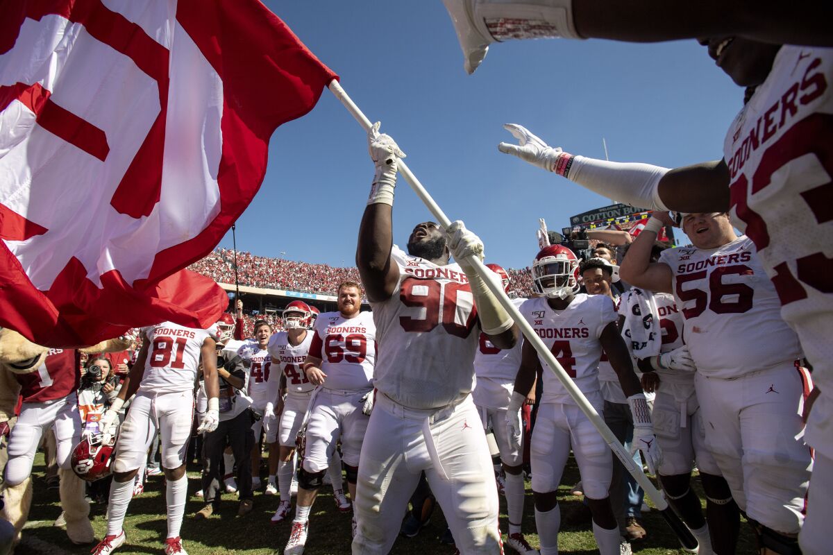 FILE - In this Oct. 12, 2019, file photo, Oklahoma defensive lineman Neville Gallimore (90) waves an OU flag after his team's 34-27 victory over Texas in an NCAA college football game at the Cotton Bowl in Dallas. The Texas and Oklahoma college football matchup will be a different game-day atmosphere this year with small crowds, no State Fair, a few food vendors, masks and social distancing. (AP Photo/Jeffrey McWhorter, File)