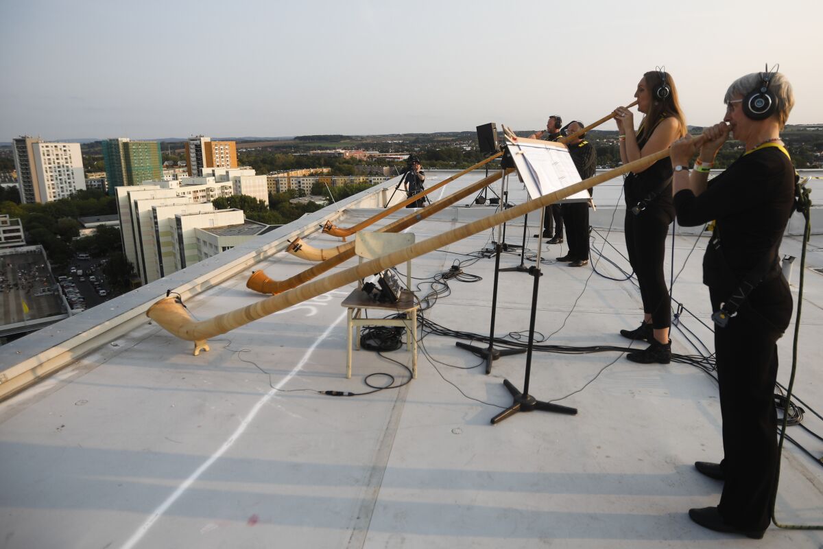 A musician with alp horns perform on the roof of an apartment block for a concert featuring distant harmonies, at a time when cultural events have been disrupted by the coronavirus pandemic, in the Prohlis neighborhood in Dresden, Germany, Saturday, Sept. 12, 2020. About 33 musicians of the Dresden Sinfoniker perform a concert named the 'Himmel ueber Prohils', The Sky above Prohlis, on the roof-tops of communist-era apartment blocs in the Dresden neighborhood Prohlis. (AP Photo/Markus Schreiber)