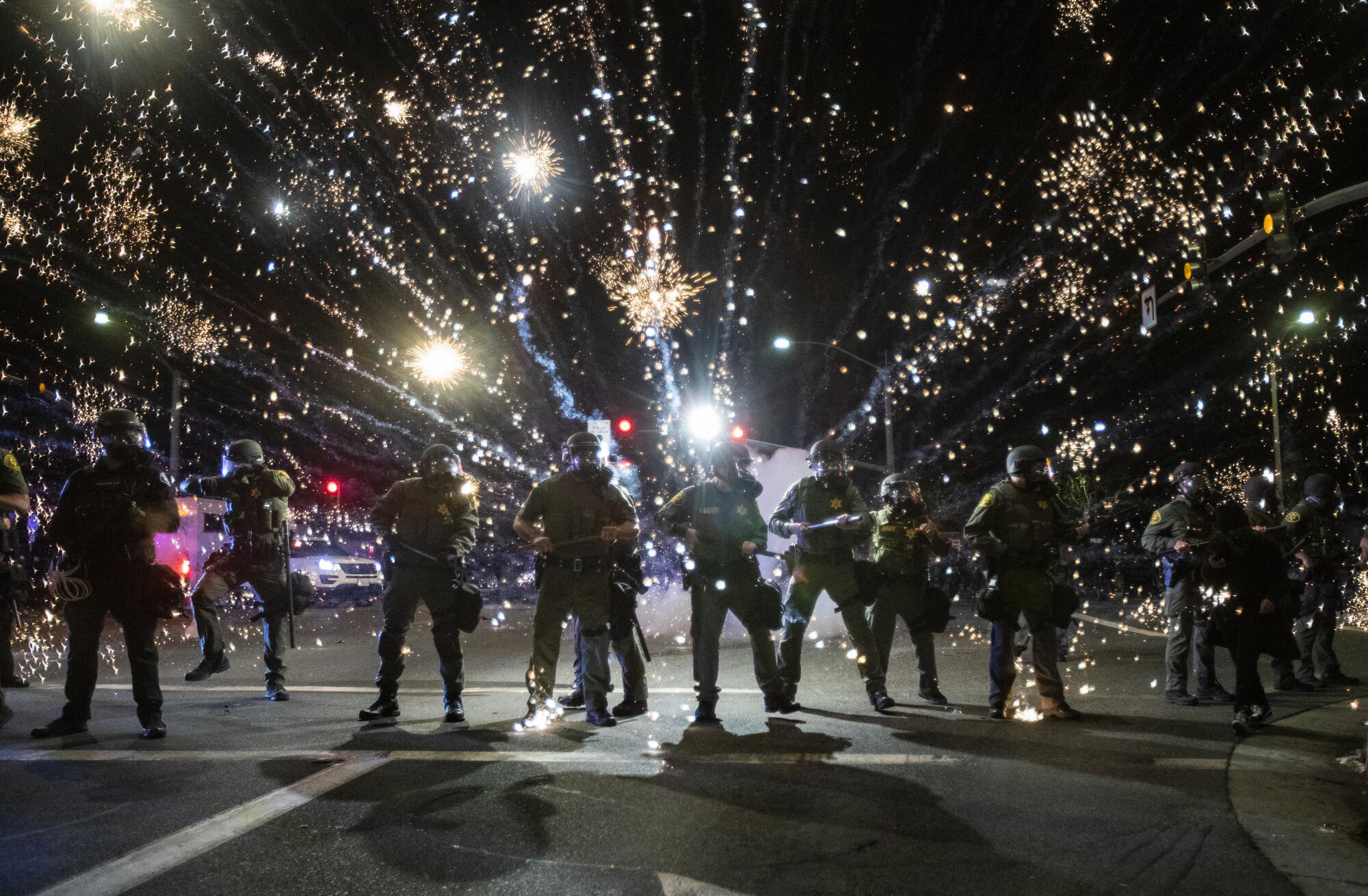 Orange County sheriff's deputies maintain a police block as a firecracker thrown by a protester explodes behind them.