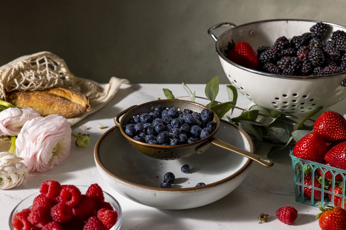 Raspberries, blueberries, strawberries and blackberries in bowls and colanders.