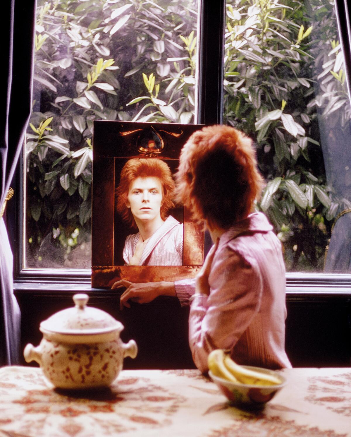 A back of a man's head and his face shown in the mirror he's looking into