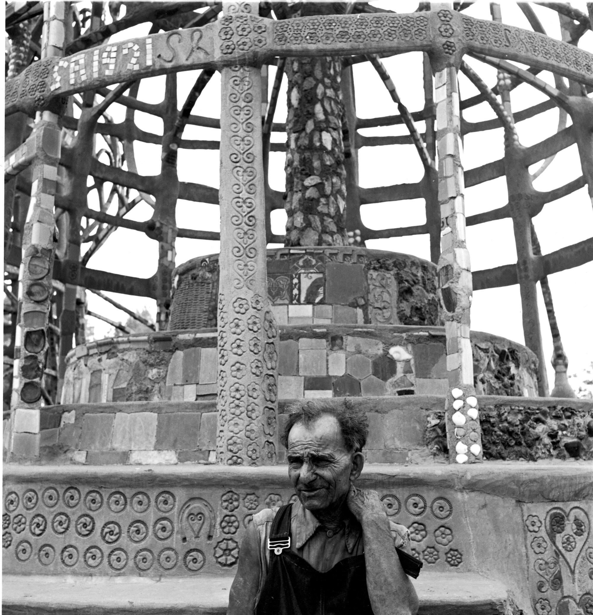 A black-and-white photo of a man in front of the Watts Towers