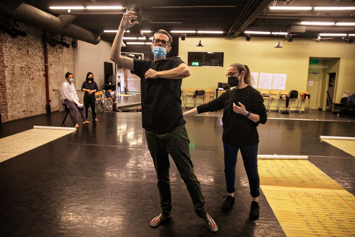 A woman corrects a man in a dance rehearsal studio. 