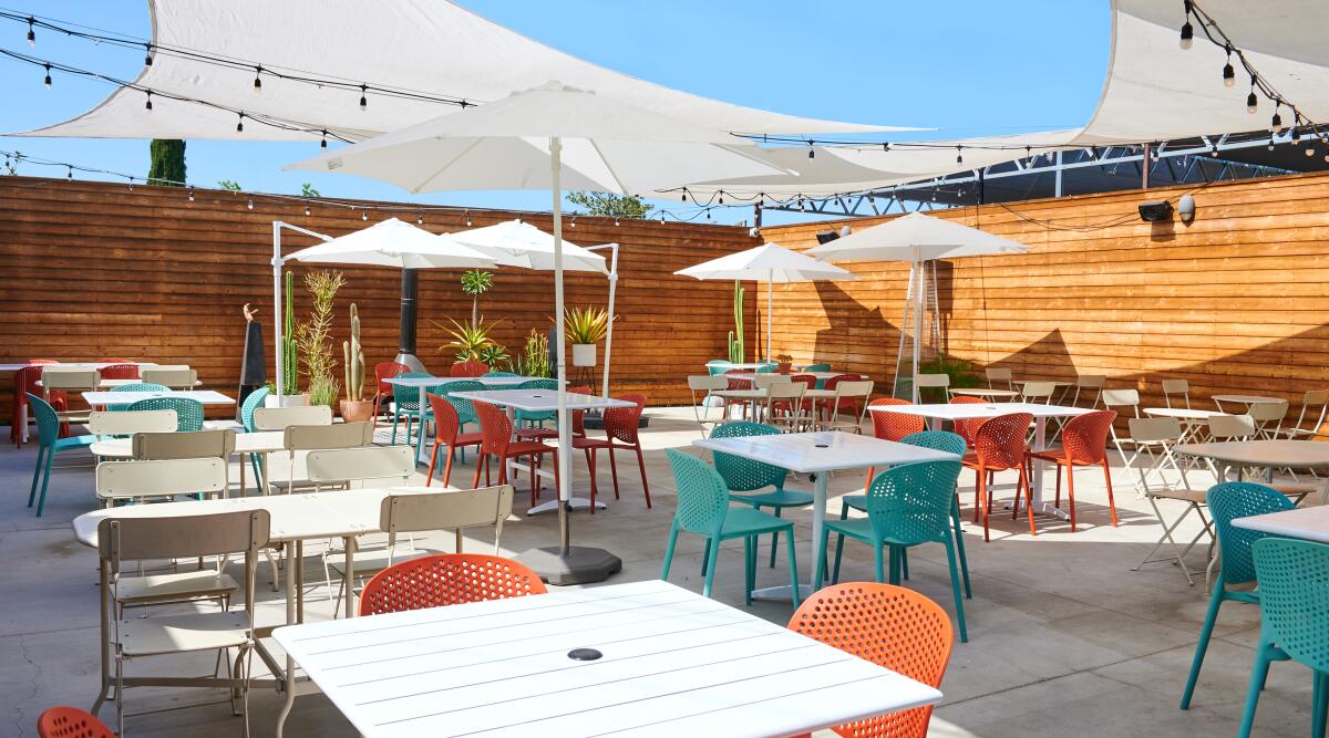 A restaurant patio with colorful chairs and white umbrellas and shade cloths.