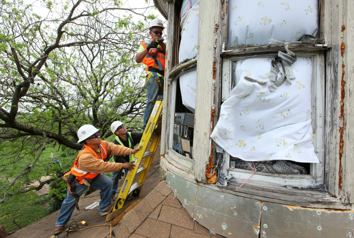 Workers with Johnson Roofing cover the windows of Carol Anne Kocian's home with sheets of plywood following the explosion in West, Texas.