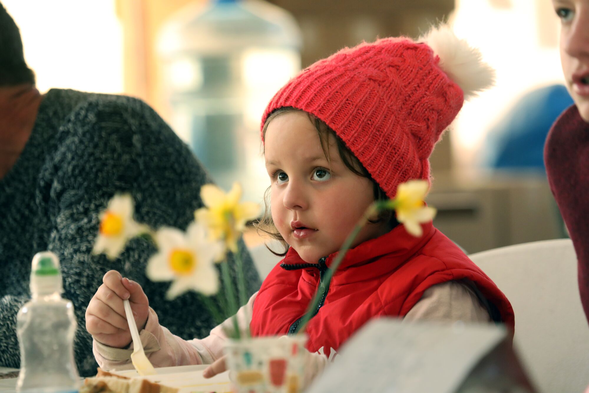 Girl in a red hat and scarf eats soup 