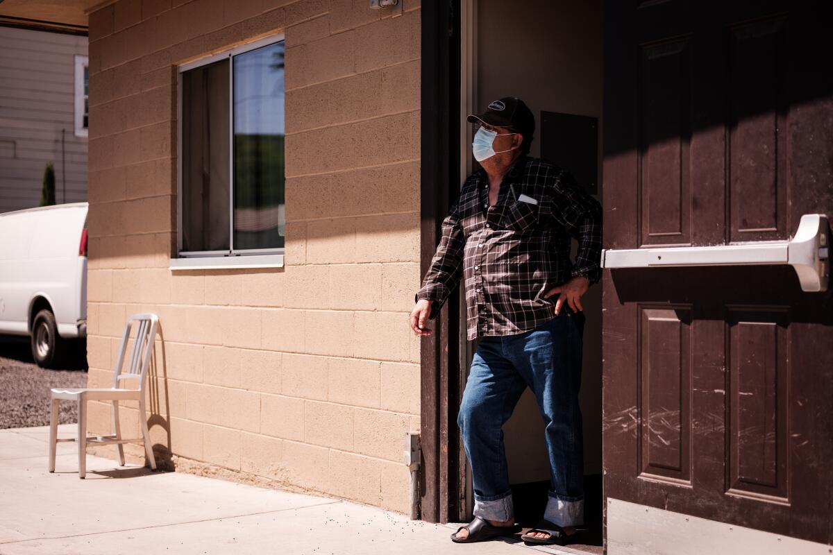 A man wearing a face mask stands in the doorway of a cinderblock building