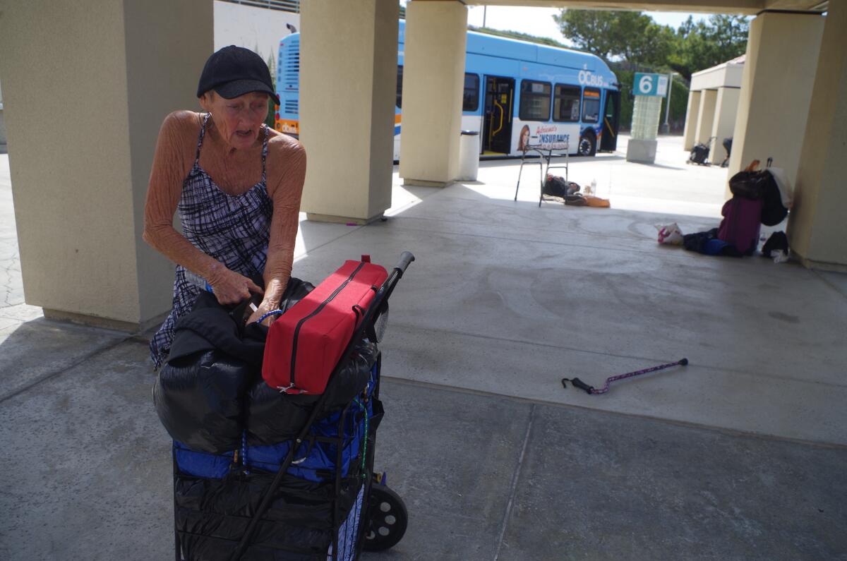 Sharon Dasher, 70, packs her belongings Thursday at the Newport Beach transit center to take a bus to Santa Ana after police the night before removed the tent she was staying in on the premises. She said she ended up sleeping on the sidewalk. She said she hoped to gather enough money to take a bus to Prescott, Ariz., where her brother lives.