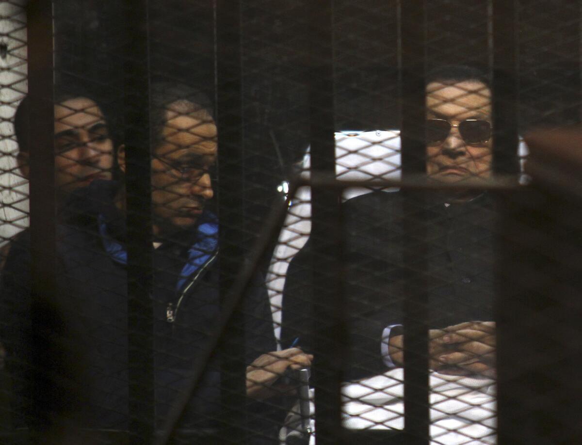 Ousted Egyptian President Hosni Mubarak lies on a gurney next to his son Gamal, second left, in the defendants cage during a court hearing in Cairo on Nov. 29, 2014.