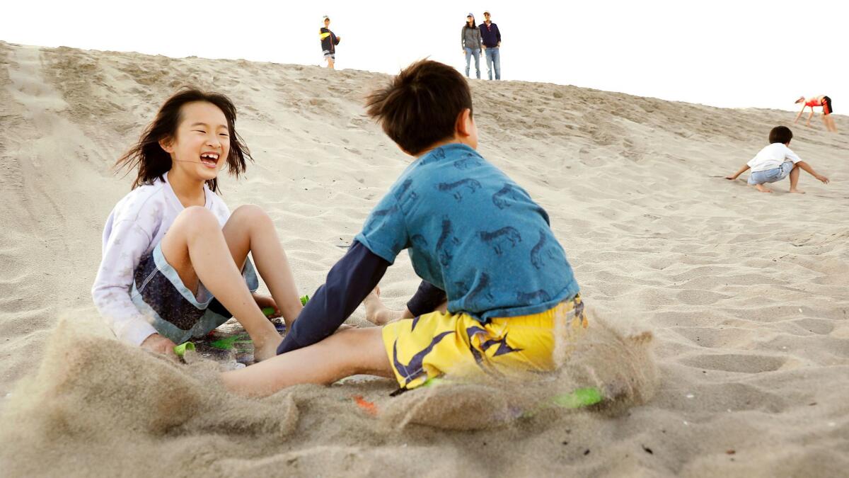 Sunnie Gao, of Sunnyvale, left, and Fredrik Wong, of South Pasadena, both 8, slide down a berm at Dockweiler State Beach on Christmas Eve.
