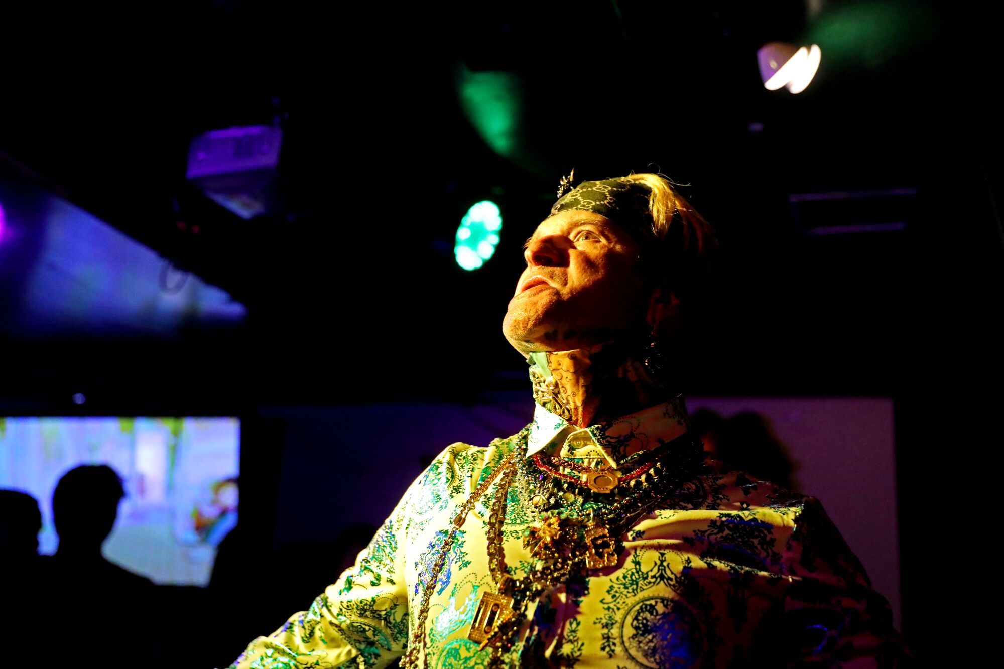 A man in a decorated collared yellow shirt and necklaces sings