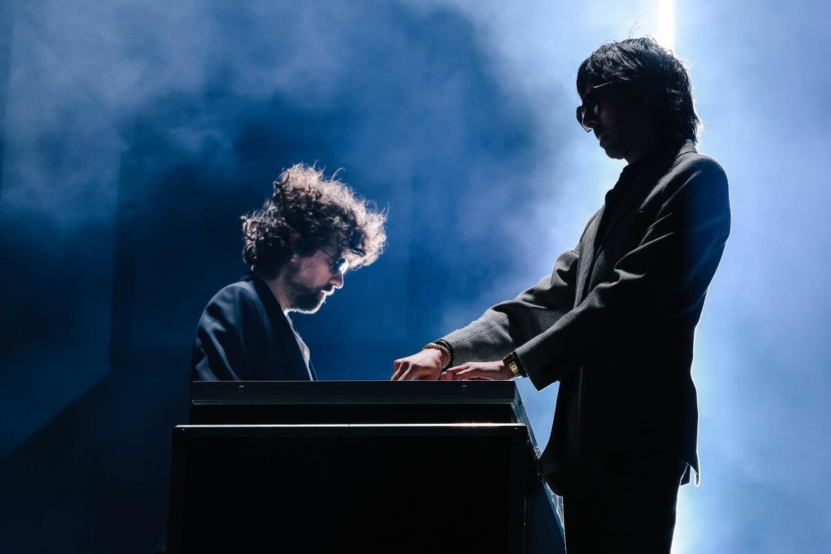 Two men in black suits playinig synthesizers on stage