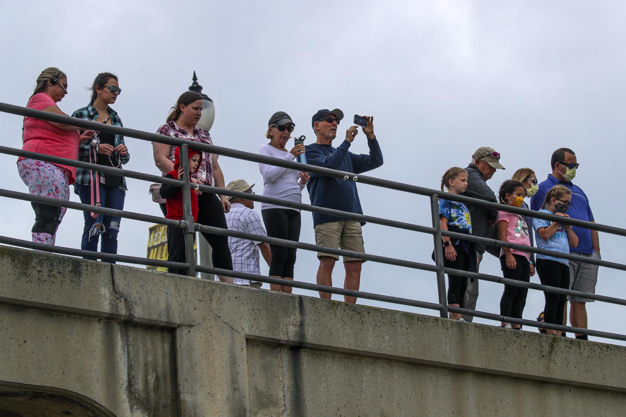 People line up on the pier, some holding up cellphones.