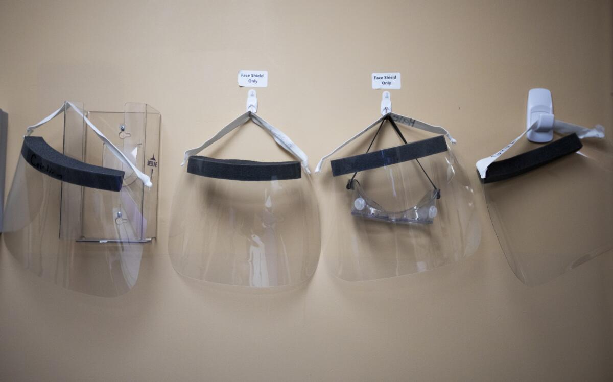 Four face shields hang in a row on a wall at a hospital in Apple Valley