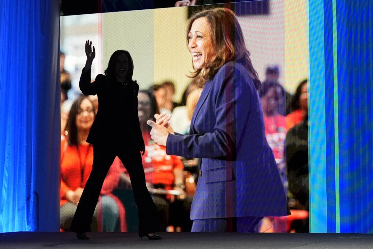 Kamala Harris is silhouetted while waving onstage with a digital screen behind her