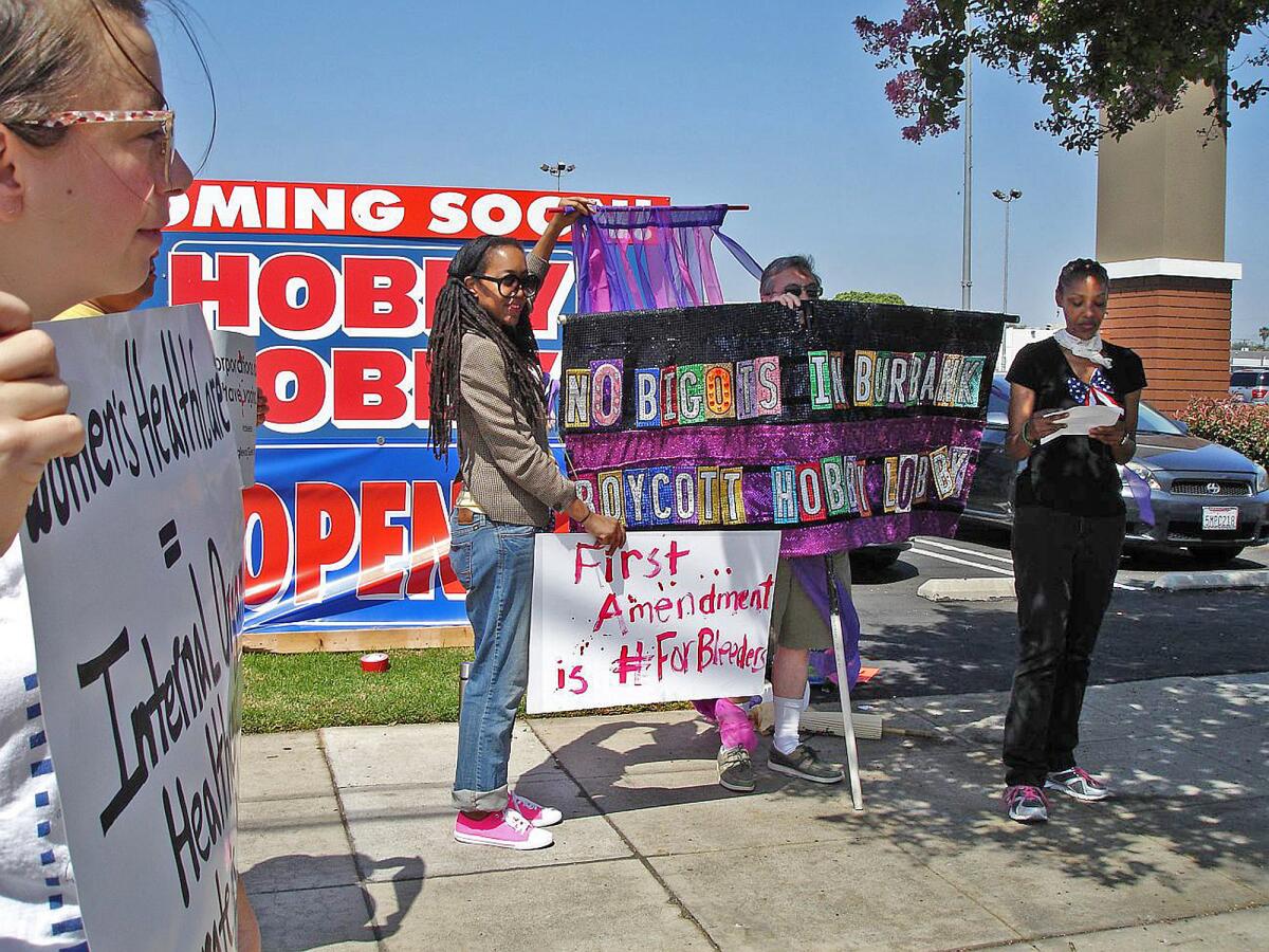 Teka-Lark Fleming, center, holds a sign while Sharon Johnson, right, of Leimert Park, reads a protest poem at a demonstration in front of the new Hobby Lobby in Burbank, which had a soft opening during on Friday, July 4, 2014.