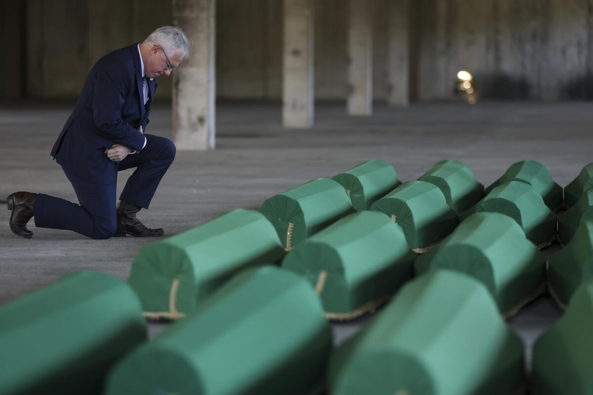 A man kneels in front of rows of small coffins