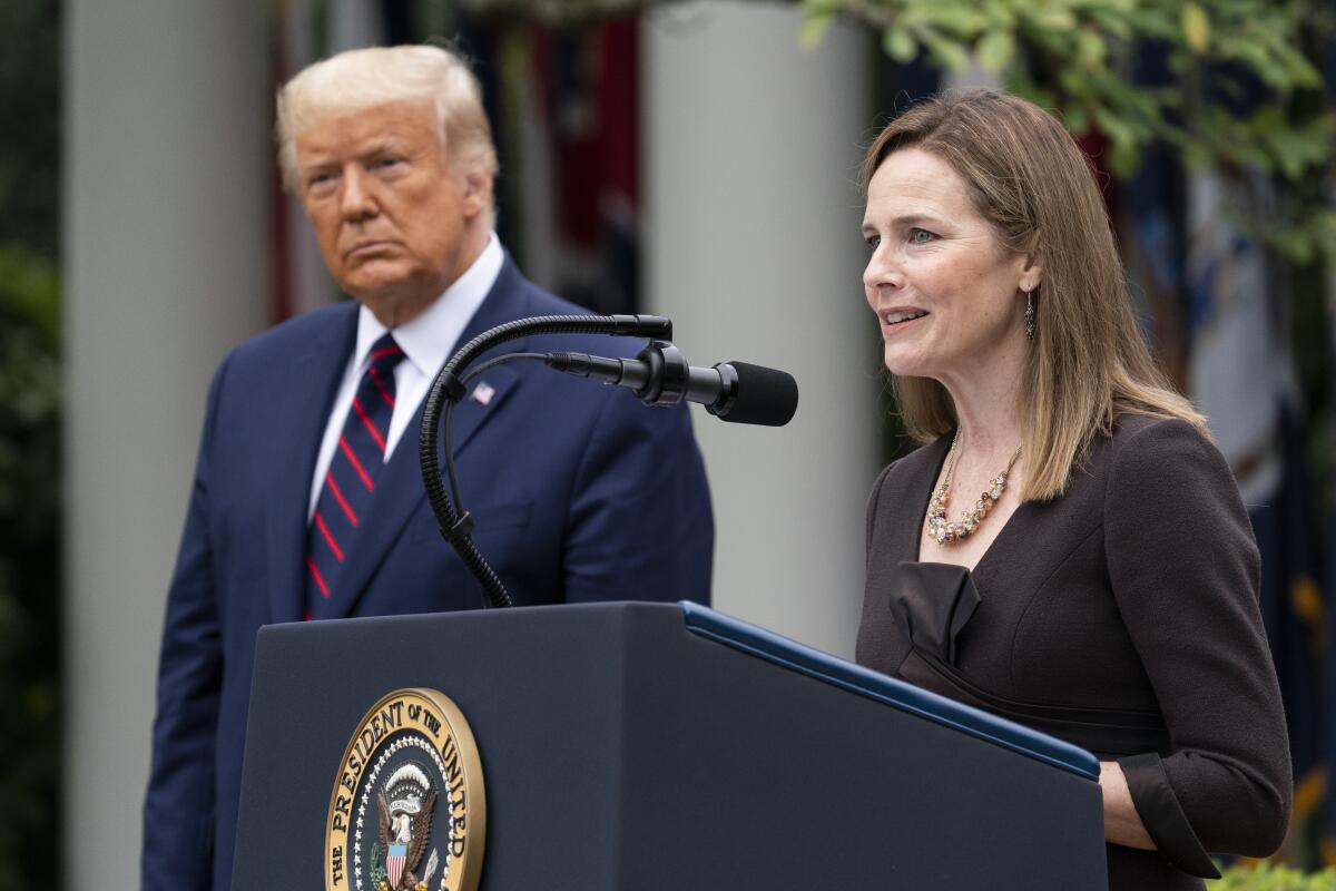 Judge Amy Coney Barrett stands at a lectern with the presidential seal next to President Trump