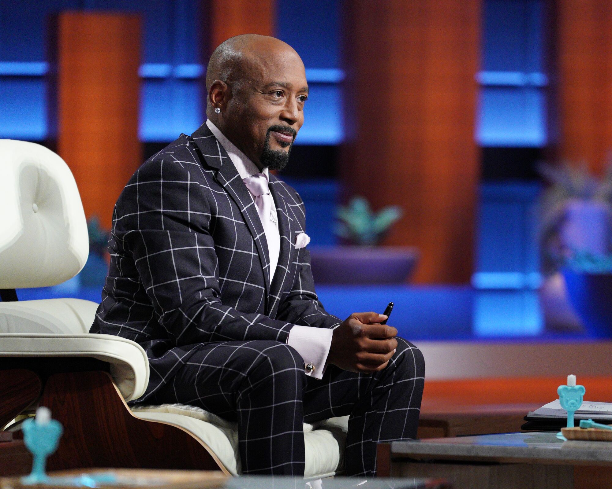 A smiling Daymond John seated in a suit on stage