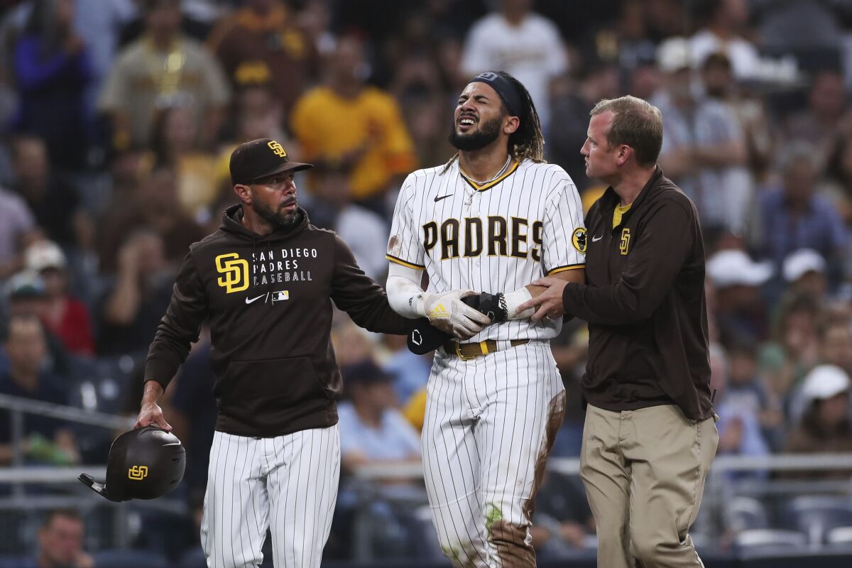 The Padres' Fernando Tatis Jr., middle, is helped off the field by manager Jayce Tingler, left, and a trainer July 30, 2021.