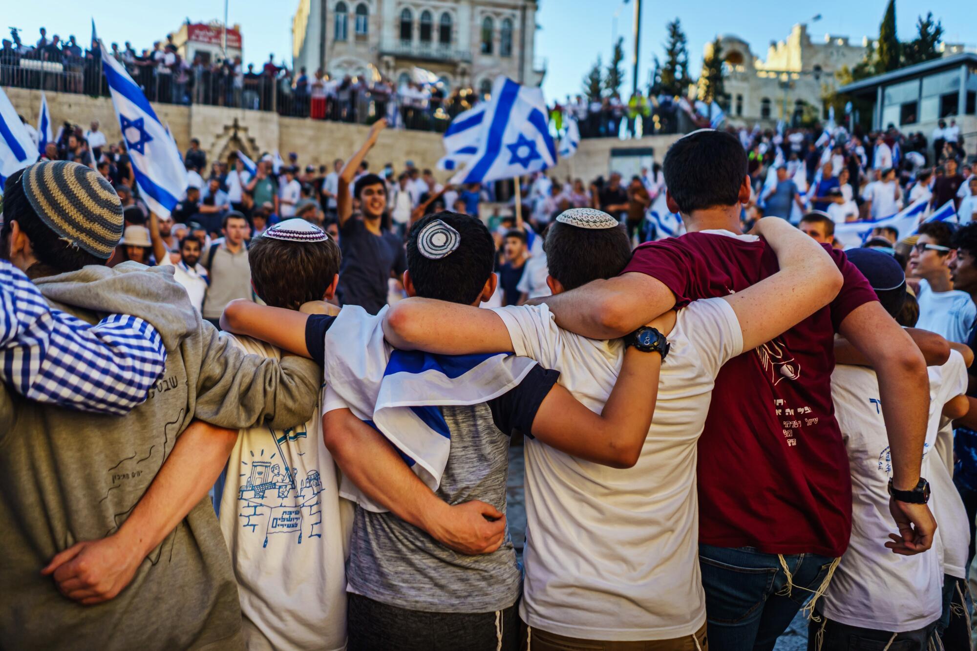 A line of young men wearing yarmulkes stand with their arms around one another.
