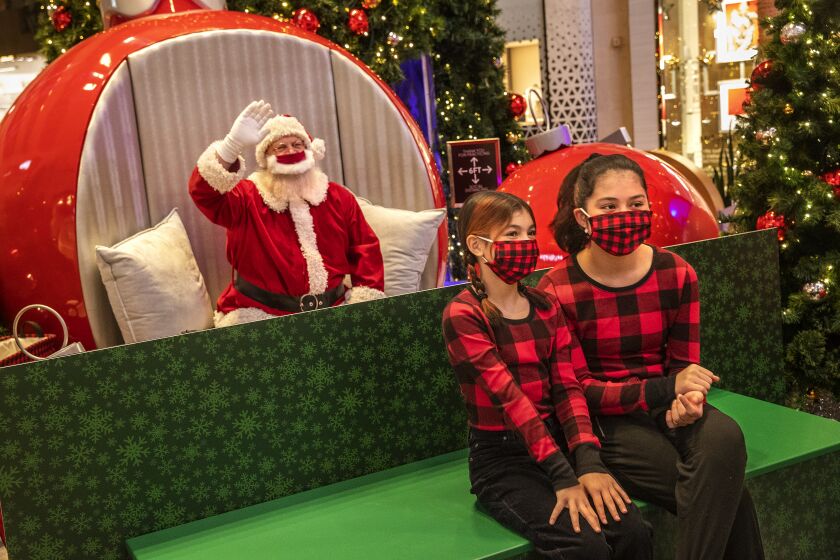 CANOGA PARK, CA - DECEMBER 02: Kelsy Tasem, 11, left, and her sister Mackenzi, 14, have their photo taken with Santa Claus, Jeffrey Fast, while social distancing as protection against the coronavirus during a visit to the Westfield Topanga Mall in Canoga Park. (Mel Melcon / Los Angeles Times)