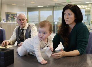 A lawyer sits beside his client at a table, while her son crawls on the table.